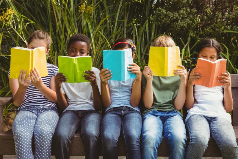 five children holding books cover their faces