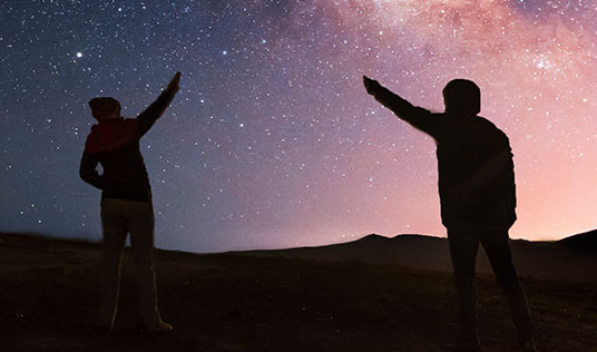 Two people pointing towards the stars