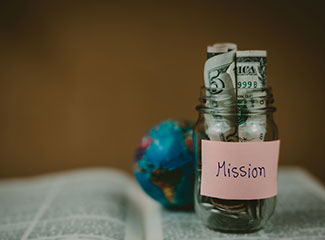money-in-a-jar-labeled-mission-next-to-a-small-globe-on-top-of-a-bible